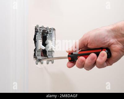 Male electrician repairing wall light switch panel. Handyman using screwdriver to install screw on light switch. Stock Photo