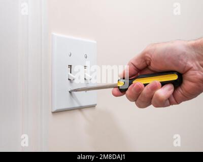 Male electrician repairing wall light switch panel. Handyman using screwdriver to install screw on light switch. Stock Photo