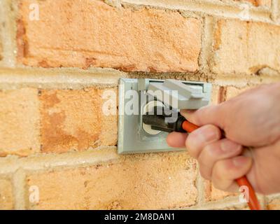 Man plugging in a power cord and then unplugging it from an outdoor electrical outlet. Dual covered outdoor power sockets on brick wall. Stock Photo