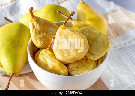 Bright yellow whole dried pears in the white bowl and fresh fruit on the wooden background close up. Stock Photo