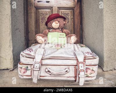 A stuffed toy teddy bear sitting on a old travel suitcase and holding a journal in his hands. Travel concept.. Stock Photo