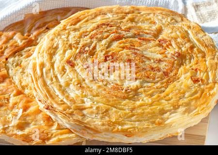 Traditional homemade Tajik Fatir (layered flat bread) with cheese and onion on light wooden background close up. Stock Photo