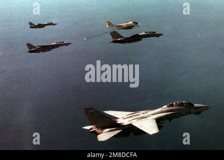 As his wing man holds position ahead, a Fighter Squadron 14 (VF-14) F-14A Tomcat aircraft moves in to receive fuel from an Attack Squadron 75 (VA-75) KA-6D Intruder aircraft. The aircraft are flanked by two Figher Squadron 32 (VF-32) Tomcat aircraft, upper left and lower right. All five aircraft are assigned the aircraft carrier USS JOHN F. KENNEDY (CV 67) which can be seen just to the left of the Intruder aircraft. Country: Atlantic Ocean (AOC) Stock Photo