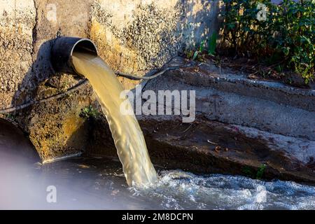 Wastewater sewage pipe dumps the dirty contaminated water into the river. Water pollution, environment contamination concept. Stock Photo