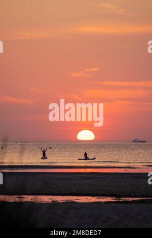 A vertical shot of people sailing on the calm sea and showing an oar at a bright red sunset Stock Photo