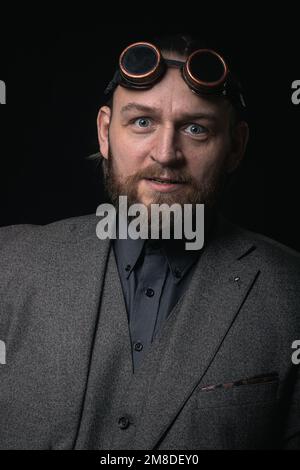 charismatic man in a classic suit and steampunk goggles on a black background stylish Portrait Stock Photo