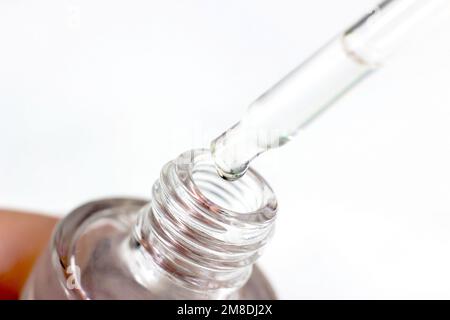 The pipette dropping a transparent liquid into dropper bottle on light background close up. Stock Photo