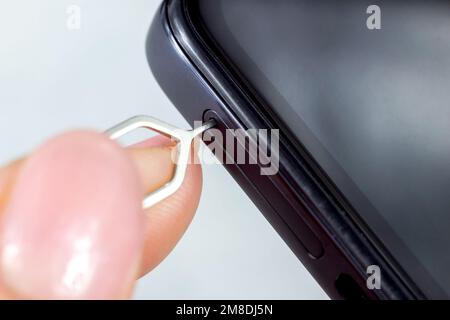 Woman hands pulling out the phone sim card tray from the smartphone with the help of edgector close up. Stock Photo