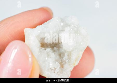 Woman hand holding shiny white crystal Agate on light background close up. Stock Photo