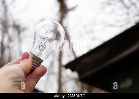An incandescent light bulb in the hands of a girl against the sky, a vozli at home, people without light, light Stock Photo