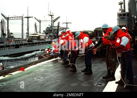 Crew members aboard the amphibious transport dock USS DUBUQUE (LPD-8) pull in a messenger line as their vessel conducts underway replenishment operations with the fleet oiler USNS HASSAYAMPA (T-AO-145). The ships are en route to the Middle East in support of Operation Desert Shield. Subject Operation/Series: DESERT SHIELD Country: Unknown Stock Photo