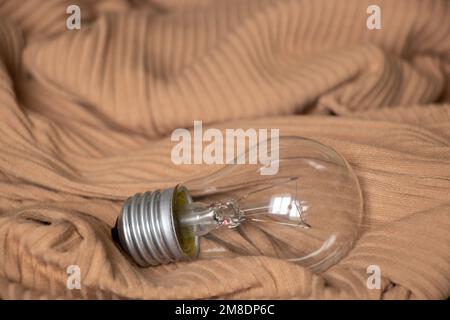 An incandescent lamp lies on a beige knitted fabric, light Stock Photo