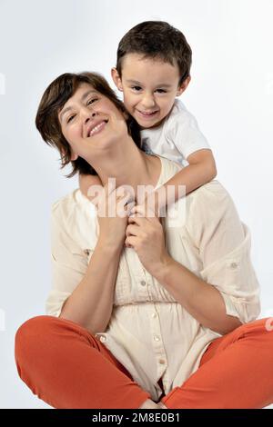 Little boy hugs his mother from behind, both look and smile at camera. Mother's day concept Stock Photo