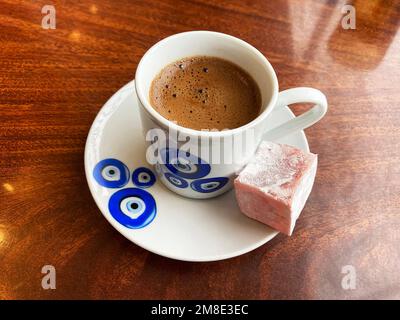 Traditional Turkish coffee cup on plate, and Turkish delight lokum on a brown wooden table. Turkish blue eye nazar symbol on a porcelain cup and plate Stock Photo