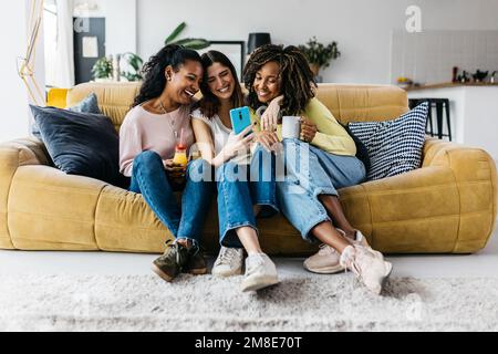 Three happy multiracial young women friends having fun using mobile phone Stock Photo