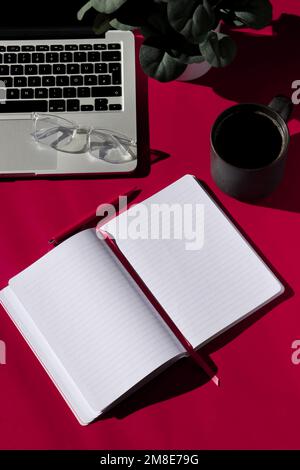 flat lay composition of empty notebook, coffee, computer and glasses on magenta background  Stock Photo