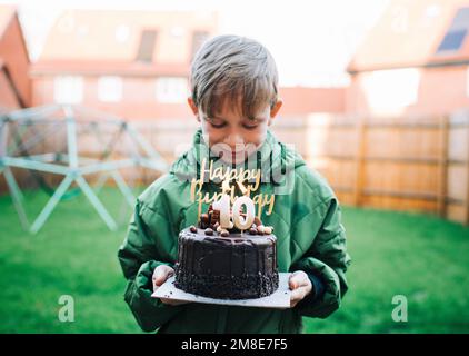 boy happily holding his 10th birthday cake with candles at home Stock Photo