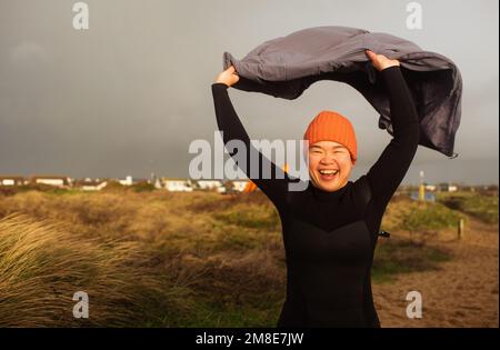 Asian woman holding her coat in the wind running to the sea Stock Photo