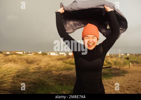 Asian woman running into the sea with her coat blowing in the wind Stock Photo