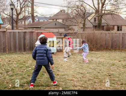 A father plays soccer with children in yard by chicken coop Stock Photo