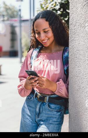Latin university student woman smiling and using her smartphone outside the campus in free time Stock Photo