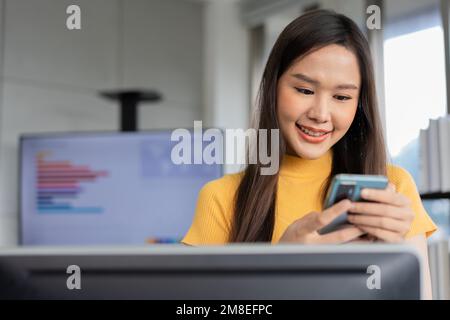 Portrait happy young programmer Asian woman work at start up technology office and using smartphone and testing mobile application and excited in succ Stock Photo