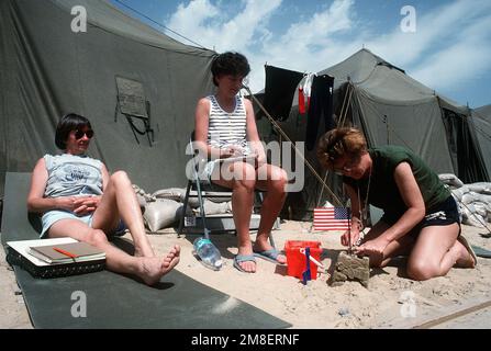 LT. Judy Fingerhut, left, and LT. Donna Delaney watch as LT. Sharon Donley builds a sand castle outside their tent at Fleet Hospital 15. The three are nurses at the hospital, which was established to support Operation Desert Shield and Operation Desert Storm. Subject Operation/Series: DESERT STORM Country: Saudi Arabia (SAU) Stock Photo
