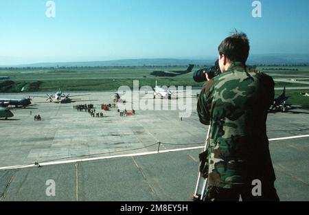 Photographer's Mate 3rd Class Klein uses a tripod-mounted Bronica camera and telephoto lens to document a ceremony during the Maritime Patrol Aircraft Conference. Two Atlantic long-range maritime patrol aircraft are among the planes parked on the airfield while a C-5A Galaxy aircraft is parked on the runway in the background. Base: Naval Air Station, Sigonella State: Sicily Country: Italy (ITA) Stock Photo