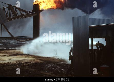 Firefighters from the Boots and Coots Oil Well Firefighting Company pour water on a blazing well after capping it in the aftermath of Operation Desert Storm. The well, situated in the Ahman Oil Fields, is one of many set afire by Iraqi forces prior to their retreat from Kuwait.. Subject Operation/Series: DESERT STORM Base: Ahman Oil Fields Country: Kuwait(KWT) Stock Photo