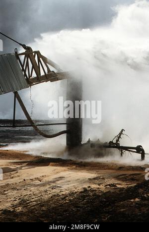 Firefighters from the Boots and Coots Oil Well Firefighting Company pour water on a well after capping it in the aftermath of Operation Desert Storm. The well, situated in the Ahman Oil Fields, is one of many set afire by Iraqi forces prior to their retreat from Kuwait.. Subject Operation/Series: DESERT STORM Base: Ahman Oil Fields Country: Kuwait(KWT) Stock Photo