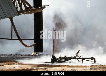 Firefighters from the Boots and Coots Oil Well Firefighting Company use a crane to remove a capping device after extinguishing a burning oil well in the aftermath of Operation Desert Storm. The well, situated in the Ahman Oil Fields, is one of many set afire by Iraqi forces prior to their retreat from Kuwait.. Subject Operation/Series: DESERT STORM Country: Kuwait(KWT) Stock Photo