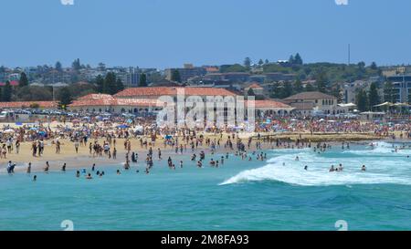 Waves and surf crash onto the sand at a busy Bondi Beach near Sydney on a perfect summer day with the iconic bathing pavilion in the background Stock Photo