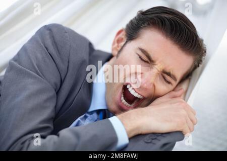 In need of a vacation. A young businessman yawning while lying on a hammock. Stock Photo