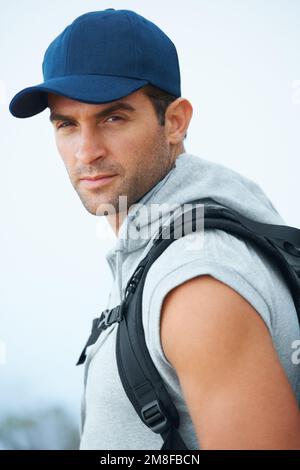 He has an adventurous glint in his eyes...Handsome young hiker wearing a baseball cap looking straight at the camera. Stock Photo