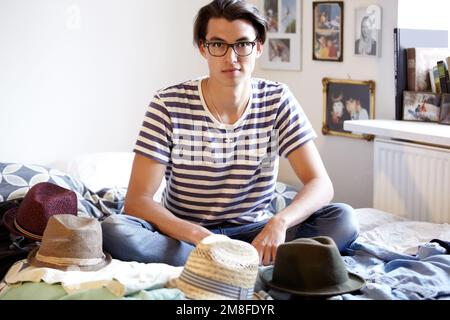 Hes proud of his style. Trendy young guy surrounded by his hat collection. Stock Photo
