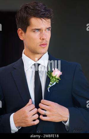 Stylish on his big day. A handsome groom wearing a pink rose on his jacket isolated on a black background. Stock Photo