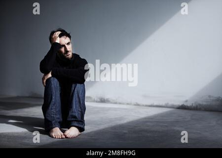 Hes been suffering from depression lately. A young man sitting on the ground with his hand on his head. Stock Photo