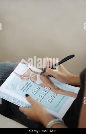 Unrealistic expectations. a young woman suffering from anorexia reading a self-help book about a celeb diet. Stock Photo