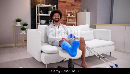 Young Man With Broken Leg Sitting On Sofa Stock Photo