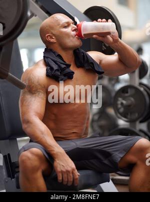 Keeping his energy levels up. a male bodybuilder drinking a protein shake while sitting on a weight bench at the gym. Stock Photo