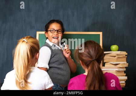Sharing her smarts with her schoolmates. Portrait of a cute girl teaching her two friends something using the chalkboard i class. Stock Photo