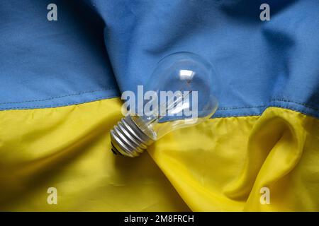 An incandescent lamp lies on the flags of Ukraine, people without light in Ukraine due to Russian missile attacks, war, crisis Stock Photo
