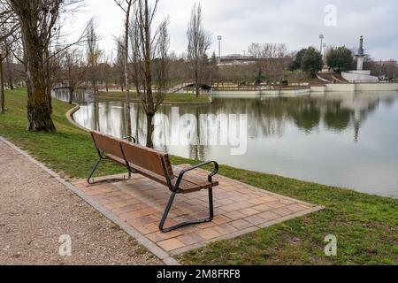 Wooden bench to sit and rest in a public park overlooking the crystal clear lake. Stock Photo
