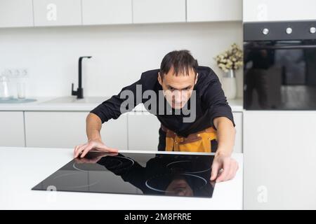 Man electrical repairs kitchen surface apartment. Installing hob in countertop. Man bought new kitchen furniture and appliances. Process installing an Stock Photo