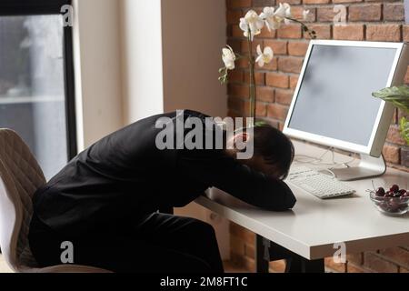 Frustrated businessman sitting on desk with hand on head in office. Stock Photo