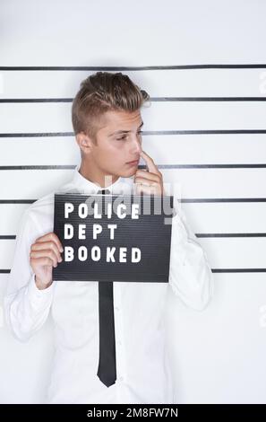 Caught in the act. Mug shot of a young man in a shirt and tie holding up a police department sign. Stock Photo