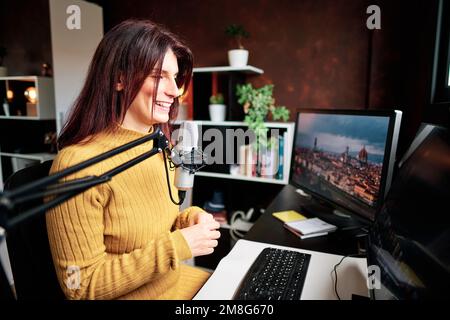 Woman smiling while recording content with microphone and computers from her home studio. Stock Photo