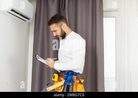 Young Technician using digital tablet and pen checking air conditioner in house room. Air Conditioning system installation and repairing concept Stock Photo