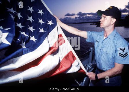 Postal Clerk 2nd Class Jamie Hughes lowers the ensign flown by the battleship USS MISSOURI (BB 63) the night before the ship's decommissioning. Base: Naval Station, Long Beach State: California(CA) Country: United States Of America (USA) Stock Photo