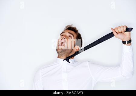 Strangled by formality. Handsome young guy yelling while being strangling himself with his neck tie. Stock Photo